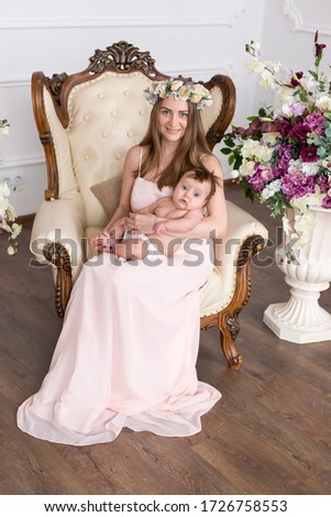 a woman in a pink dress holds a child in her arms. mother with baby. spring mommy in a wreath on a beautiful chair with a child. mothers Day