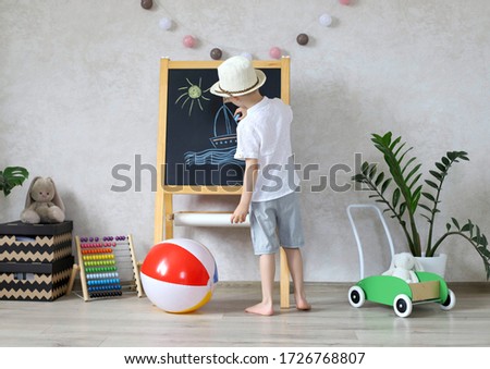 The boy draws the sea on an easel in the children's room, dreams of the sea and travel sitting at home in quarantine in isolation. 