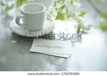 blurred abstract background in white and green, a Cup of coffee and a card with the words stay home