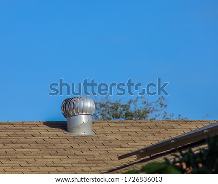 View of an aluminum internally braced wind turbine on top of a house's shingle roof.