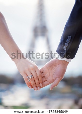 Loving couple of elegantly dressed newlyweds holding hands standing on the Trocadero opposite the Eiffel Tower in Paris
