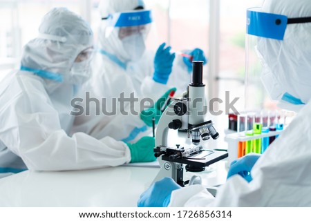 close up picture of scientist wearing personal protective equipment or ppe using microscope to do experiment about covid-19 or coronavirus vaccine in the lab. science and medical concept