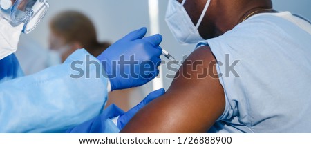 hand of medical staff in blue glove injecting coronavirus covid-19 vaccine in vaccine syringe to arm muscle of african american man for coronavirus covid-19 immunization Royalty-Free Stock Photo #1726888900