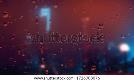 Raindrops on the window. Red and blue lights. Night city.