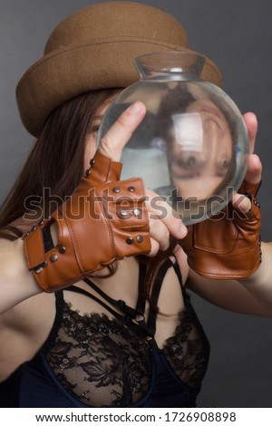 portrait of woman in Studio, in the brown hat and leather gloves Looking Through a water vessel. with Funny Distorted Eyes