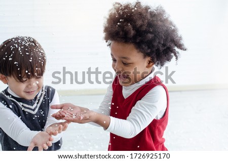Dark skinned boy and Caucasian boy having fun playing with fake snowflakes