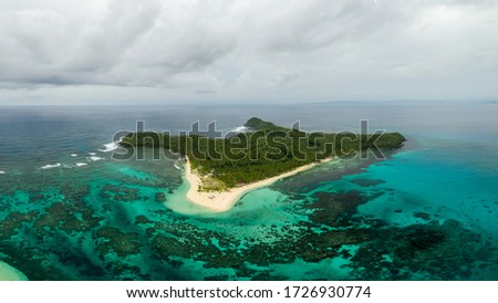 Drone picture of mamon island surounded by turquoise water, and a cloudy grey sky in the background