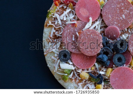 Uncooked frozen round pizza on black with fork and knife