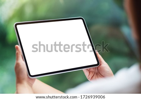 Mockup image of a woman holding black tablet pc with blank white desktop screen , green nature background
