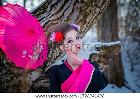 Portrait of geisha with japanese umbrella in black and pink kimomo on winter landscape background. 