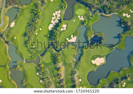 Aerial view of a golf course fairway and green with sand traps, trees and golfers. 