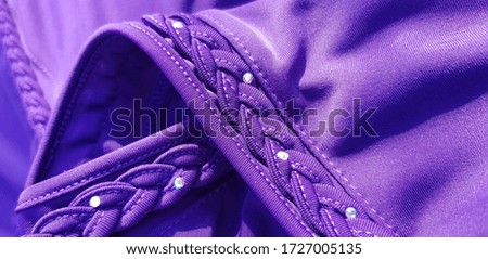 Purple synthetic fabric, decorated with a pigtail in rhinestones, in wavy folds (texture).
