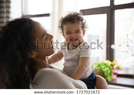 Loving young african American mother hold in arms cute funny infant toddler showing first teeth, caring happy biracial mom hug embrace smiling little baby girl child, motherhood, childcare concept Royalty-Free Stock Photo #1727021872
