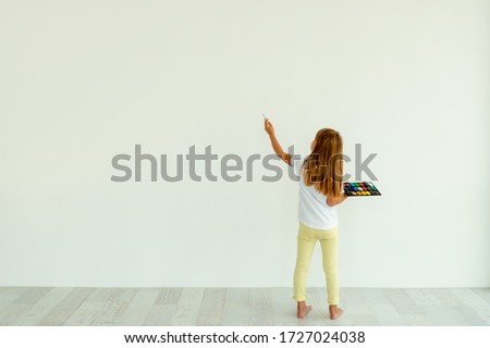 Little girl painting on white wall indoors. view from the back