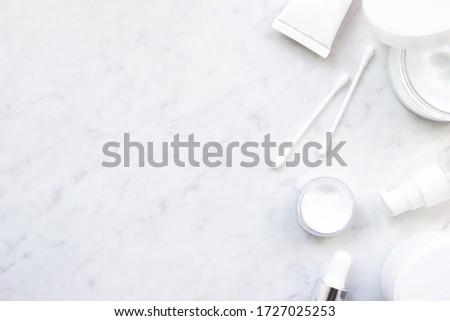 White squeeze tube, opened bottle of cream, pump bottle, dropper glass, cotton buds flat lay on marble background top view copy space. Beauty skincare, natural cosmetic, daily products. Stock photo.