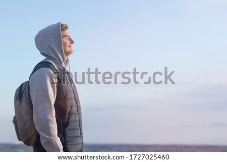 A young, handsome male guy, in the background of a clear sky, at sunset enjoys the fresh air. outside. Copy Space