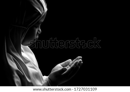 A picture of a young Asian Muslim girl praying with tranquility and faith, with the light from the studio lights from behind, with copy space.