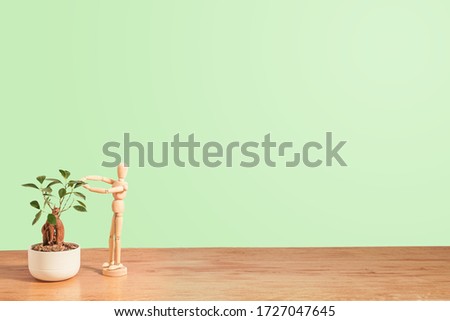 bonsai and wooden drawing mannequin takes care of it, copy space, green gradient background, ideal for ecological and green concepts                                                