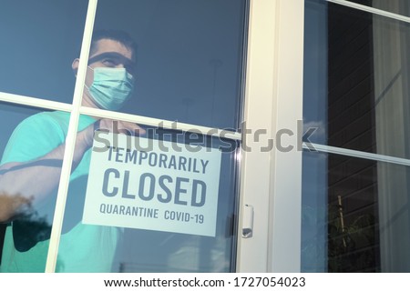 Owner of establishment glues a sign with the inscription TEMPORALLY CLOSED during coronavirus pandemic. Private business closes from the quarantine COVID-19 pandemic. Caption: temporarily closed. Royalty-Free Stock Photo #1727054023