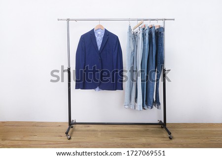 Blue suit close up with blue long sleeved shirts with row of blue jeans on hanger-wooden background 
