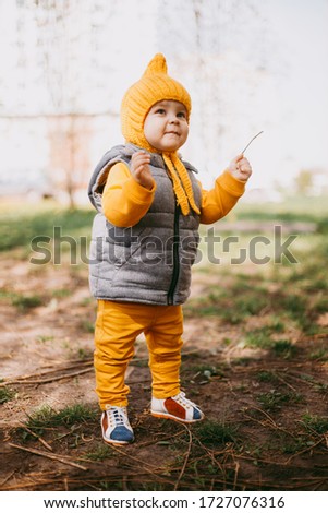 Stylish little one-year-old boy in a yellow hat, yellow pants and a gray jelly