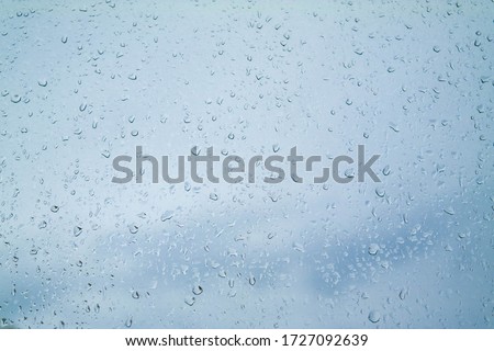 Close-up raindrops on the glass and the sky outside the window. Blue textured abstract background with water drops and rainy weather. Transparent wet non-uniform surface, condensation effect.