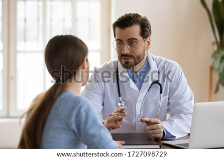 Serious Caucasian male doctor in white medical uniform talk discuss results or symptoms with female patient, man GP or physician consult woman client give recommendation at meeting in hospital Royalty-Free Stock Photo #1727098729