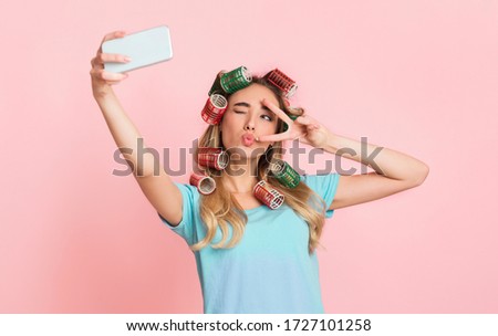 Social networks for housewife concept. Girl in curlers, make blowing kiss and winks, makes selfie