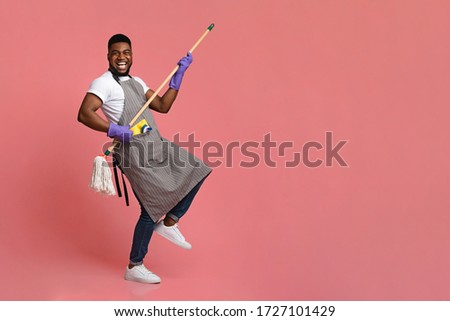 Funny African Man Using Mop Handle As Guitar, Having Fun During Cleaning. Posing Over Pink Background In Studio, Copy Space Royalty-Free Stock Photo #1727101429