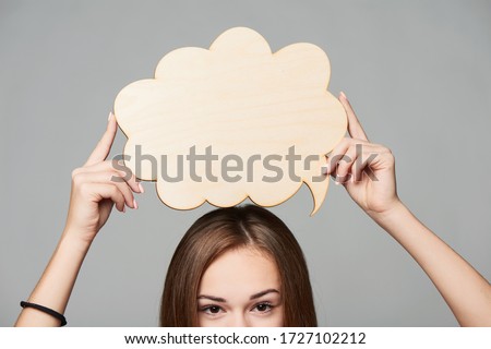 Cropped woman face holding thinking bubble above, over grey background