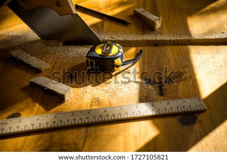 A high angle shot of a saw, a measuring tape, and a wooden ruler on some pieces of wood