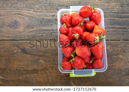 ripe strawberries in a plastic container on a table on a wooden brown background. place for text
