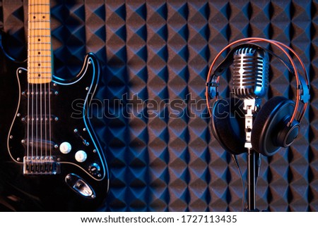 Studio condenser microphone with professional headphones and black electric guitar, on acoustic foam panel background