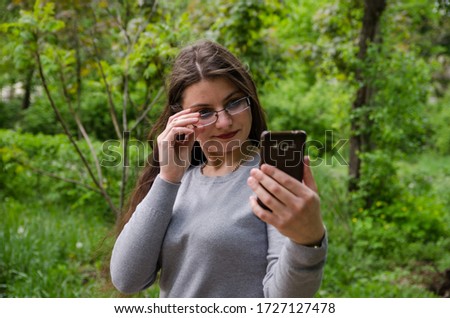 beautiful young girl in glasses looks with a phone. Green background.
