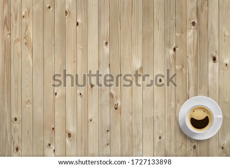 Top view picture of clear white coffee cup with smiling face from coffee bubbles put on wooden table floor. Background for flat lay design or minimalist style and copy space.