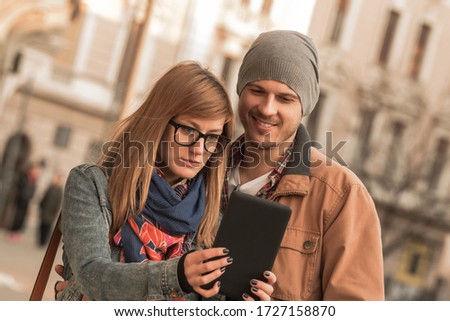 Young tourist couple using smart tablet in urban city environment for taking photos.