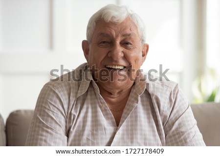 Portrait of happy mature 80s man sit on couch at home look at camera posing relaxing on weekend, smiling positive senior 70s grandfather rest on sofa at home or retirement house, show optimism Royalty-Free Stock Photo #1727178409