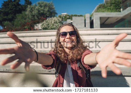 Cheerful young woman with dark curly hair enjoying holiday in city, Beautiful girl pulls hands into the camera.