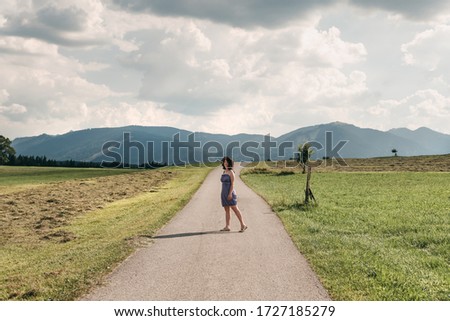 Young white woman in a blue dress and brown hat walks on the road to mountains in summer. The new way, the choice of a new road, a change of life.
