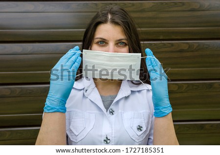 Professional doctor a young woman in blue gloves shows how to wear a medical mask.