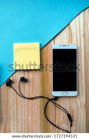 Still life, business, stationery or education concept: top image with blank pages and smartphone, headphones on a wooden and blue background, ready to be added or mock up