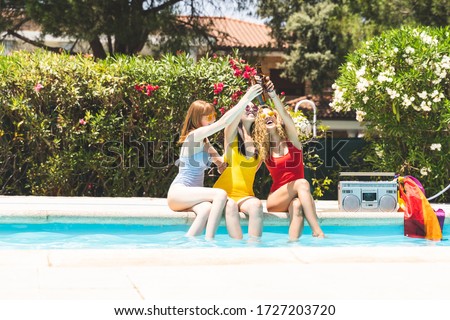 Group of Friends Having Fun in a Pool Party. Friends in the Swimming Pool. Asian , Caucasian and Blond Girls on the Edge of the Swimming Pool. Lifestyle Concept.