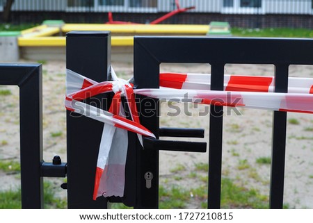 closed entrance to the Playground with white and red fencing tape .metal gate . restriction during the epidemic in Europe