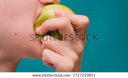 Healthy eating and healthy teeth or diet, young woman bites a fresh apple on a green screen close-up.