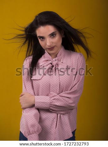 young beautiful brunette model in pink sweater,laughs and shakes his hair in the air,yellow background on the back,caressing looks very sweet camera,posing in studio