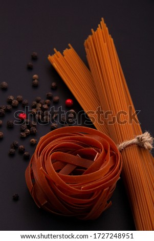 Different types of pasta and spices on a black background. Linguine, red ribbon pasta, black pepper, barberry.