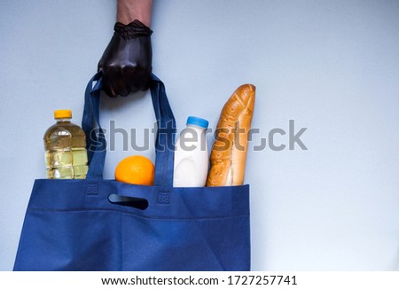 hand in a black protective glove holds a blue eco bag with products on a marine background.
