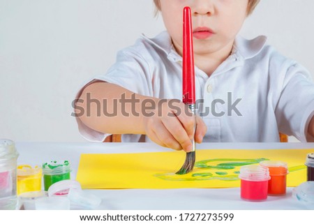 Big red paintbrush in a child's hand.  Child draws on yellow paper