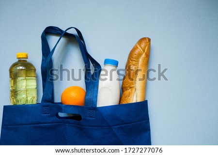 A set of food products which consists of milk, orange, sunflower oil and a baguette in a blue bag, which lies on a background of marine color. Photographed from above. Place for text.