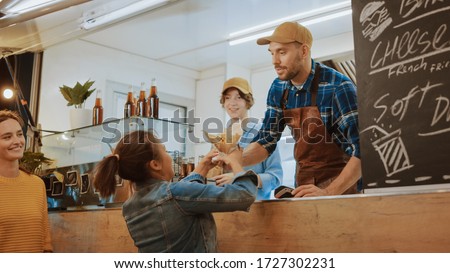 Food Truck Employee Hands Out a Freshly Made Burger to a Happy Young Female. Young Lady is Paying for Food with Contactless Credit Card. Street Food Truck Selling Burgers in a Modern Hip Neighbourhood Royalty-Free Stock Photo #1727302231